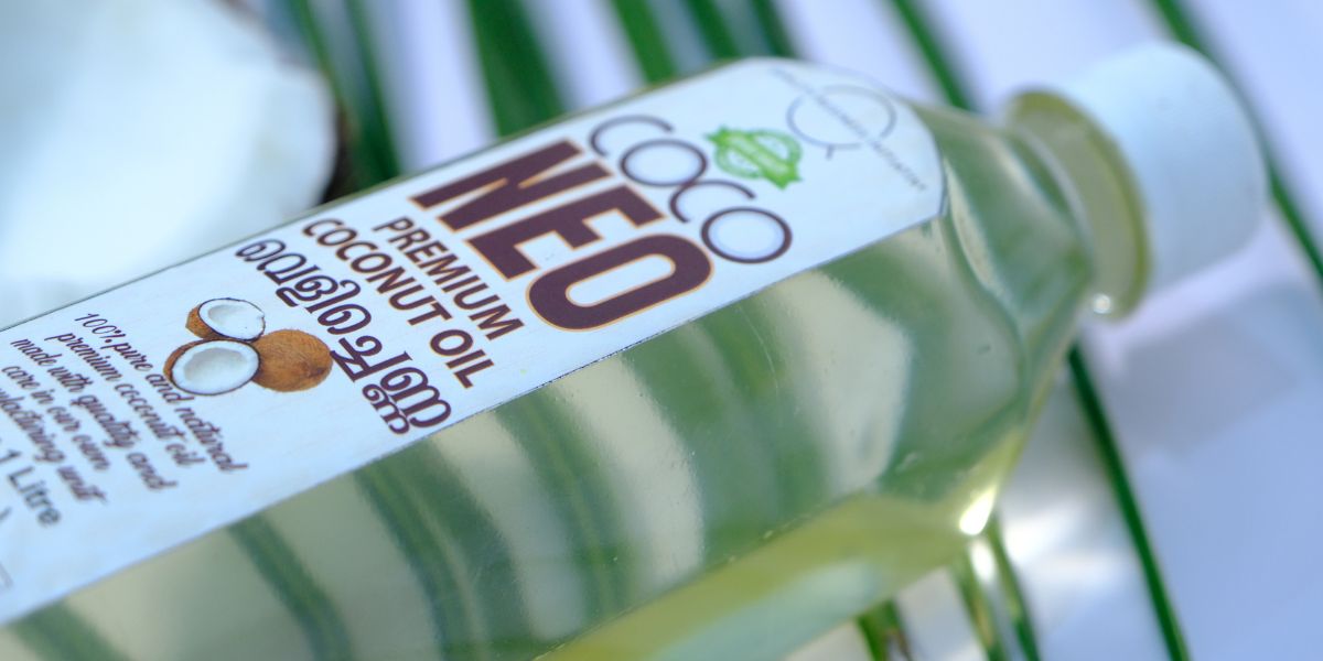 Coco Neo 1L Kerala cold pressed coconut oil bottle with coconut half and palm leaves background