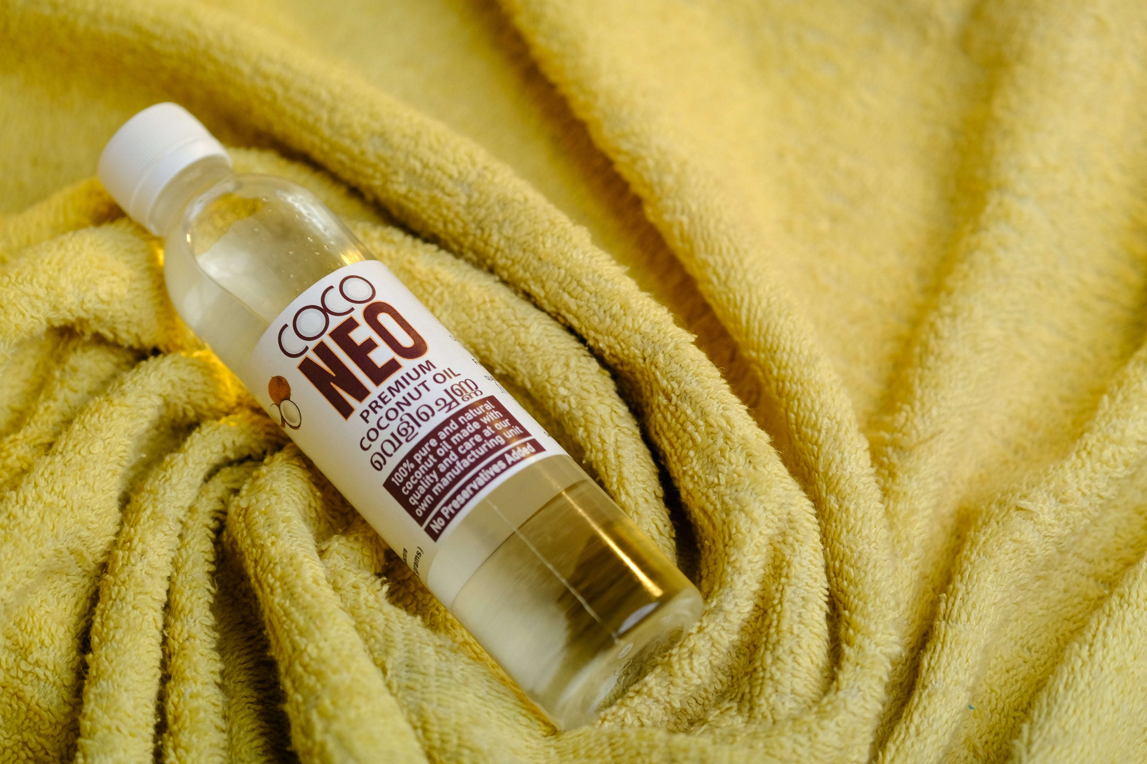 Coco Neo 100ml Kerala cold pressed coconut oil bottle displayed on a yellow towel